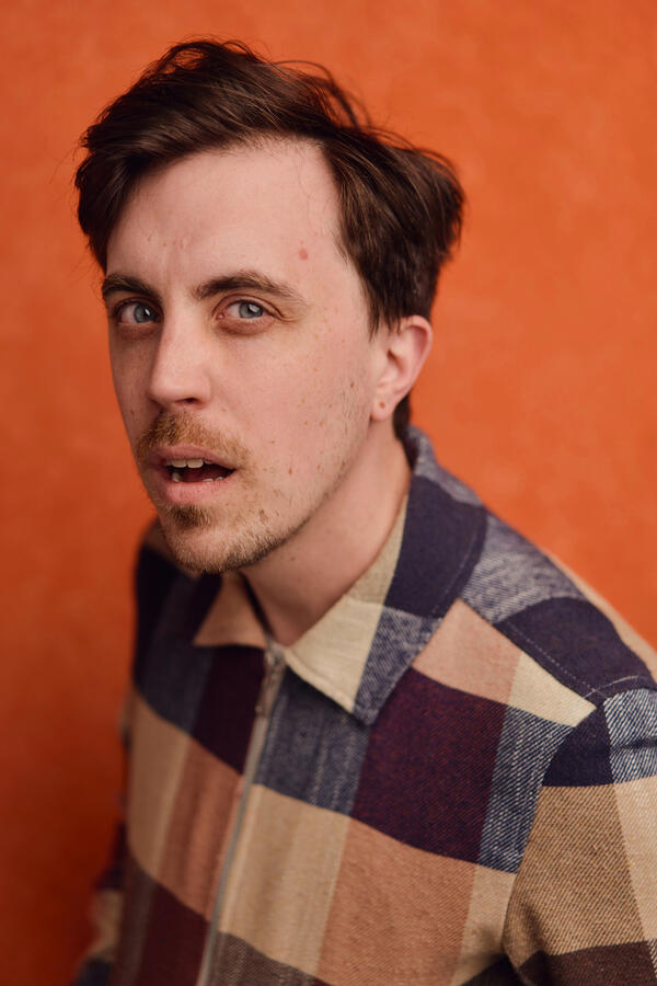 Felix Trench in a multicoloured jacket on an orange background.